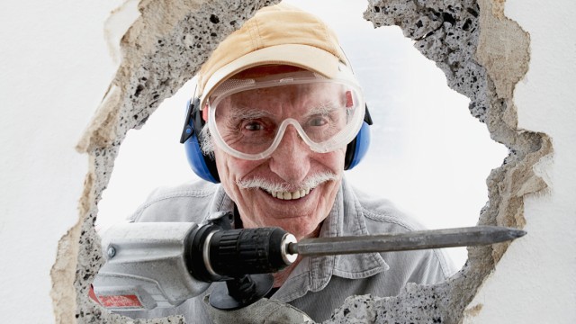 Mit dem Kopf durch die Wand - Alter Mann bricht mit Bohrmeißel durch Wand